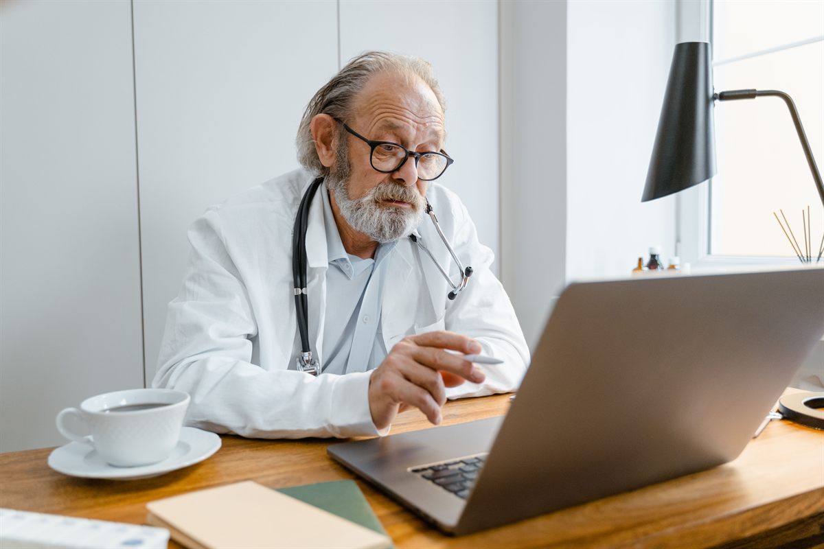 A senior doctor working on clinical systems at a laptop
