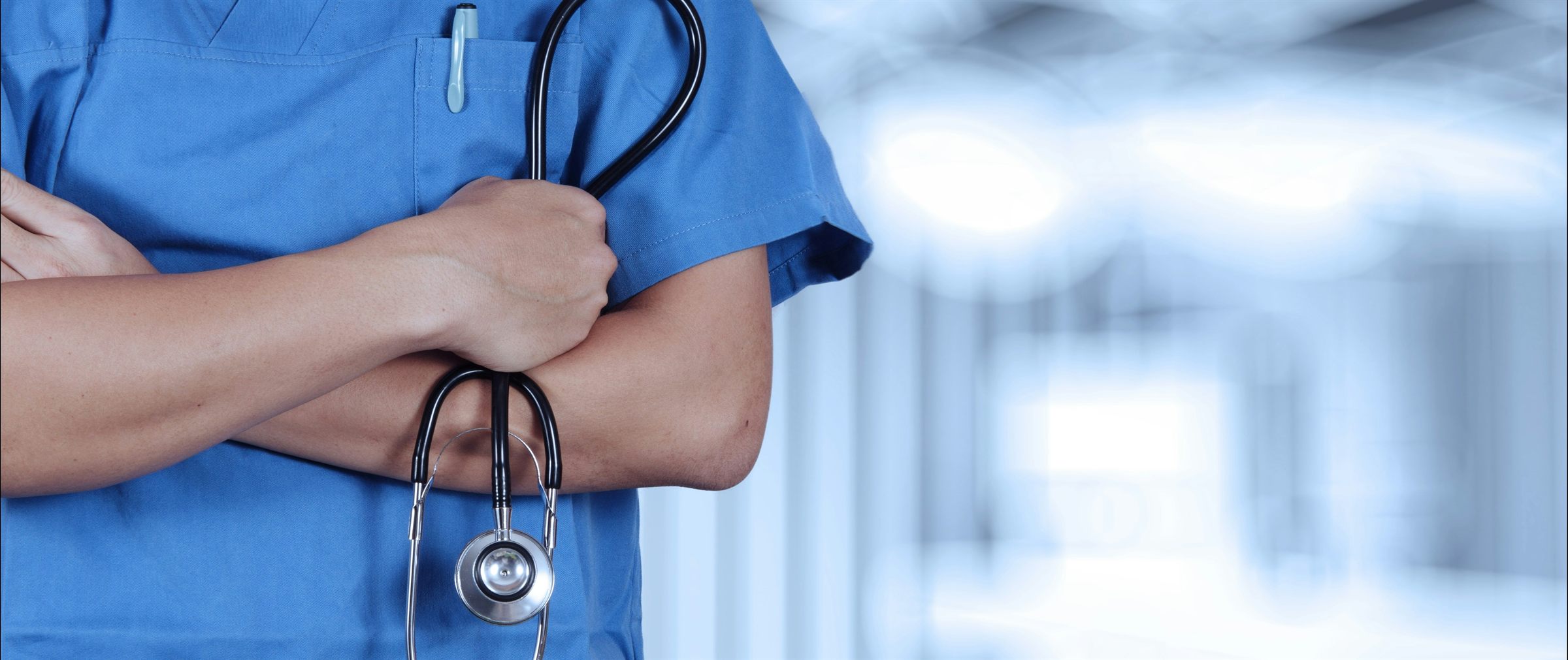 A clinician in scrubs with a stethoscope, arms folded